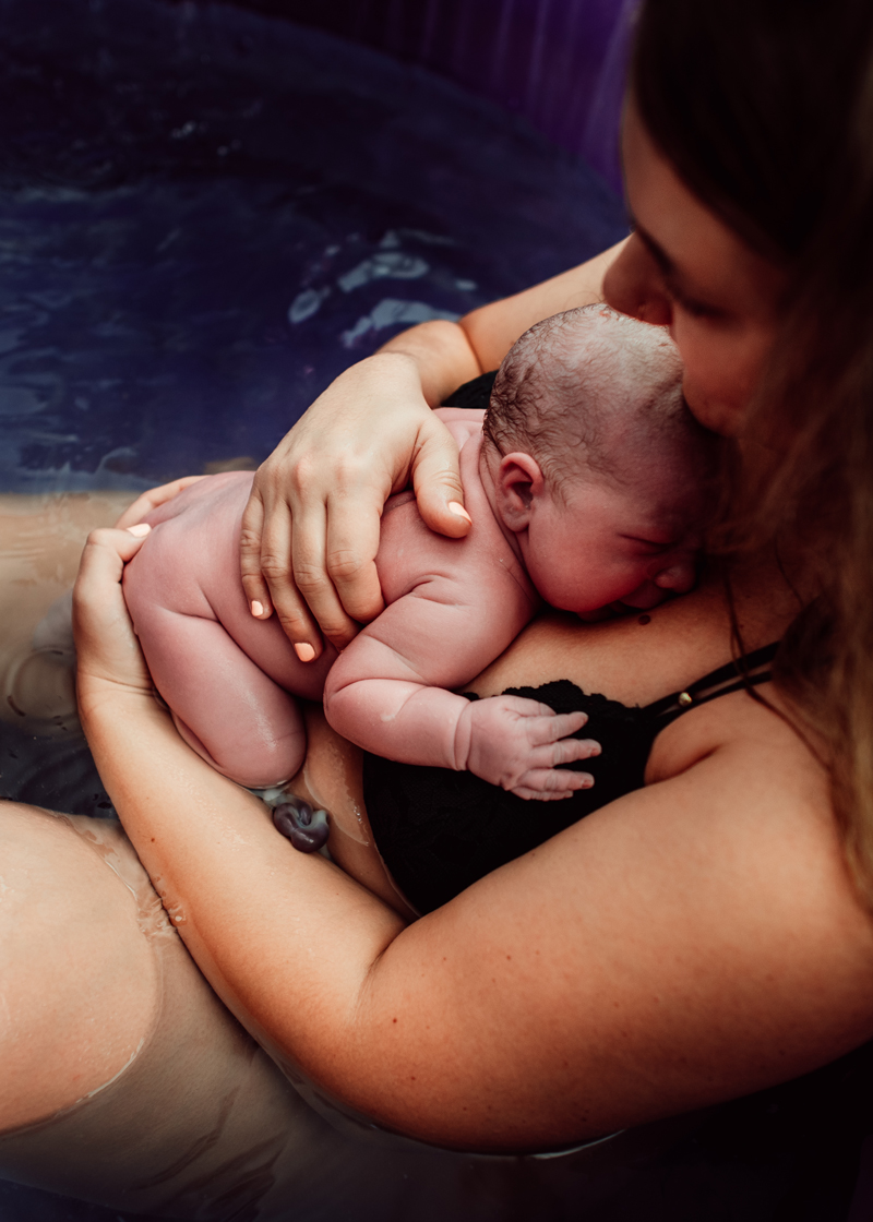 Birth Photography - woman holds newborn baby close after birth