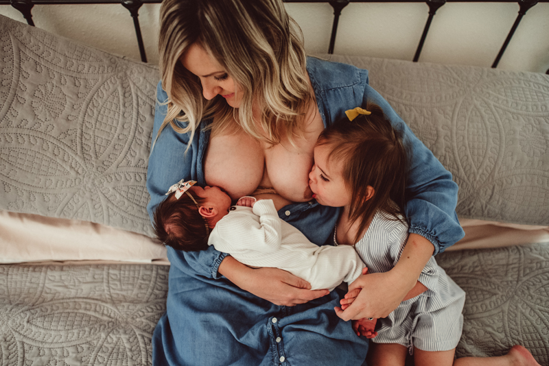 Postpartum Photography -  a woman breastfeeds both of her daughters, one a newborn baby, the other a young toddler