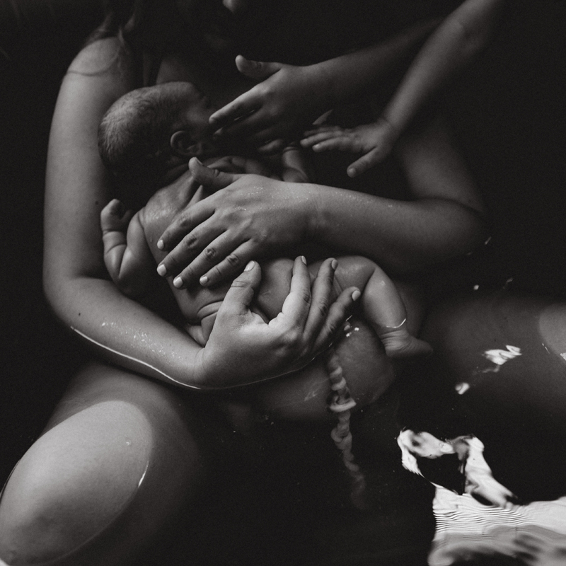 Birth Photography - woman holds onto new baby in birthing tub, umbilical cord still attached