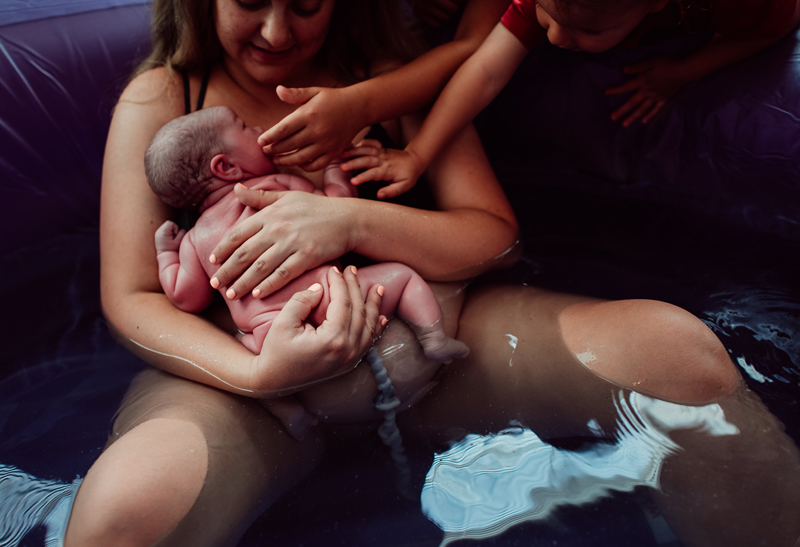 Birth Photography -woman holds baby on her chest, umbilical cord still attached within birthing pool