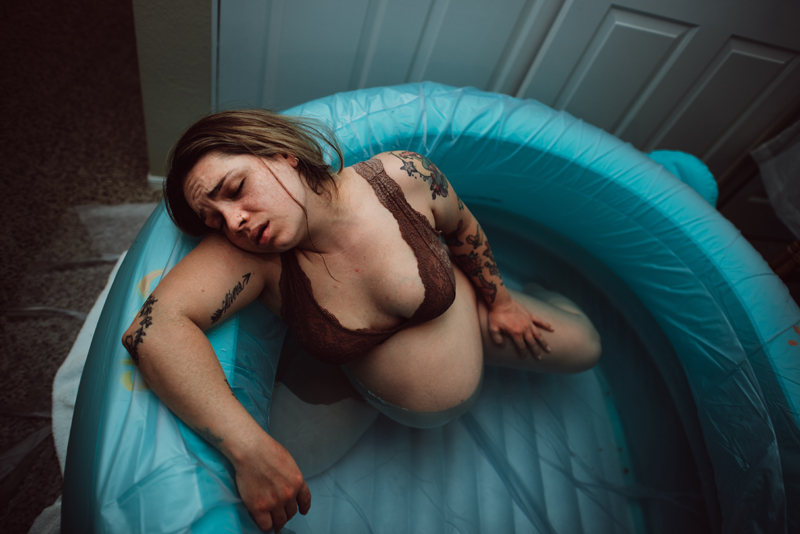 Birth Photography - tired woman lay on her arm in a birthing tub preparing for labor
