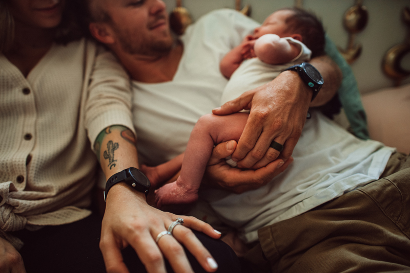 Postpartum Photography - near his wife, a man holds onto their newborn baby