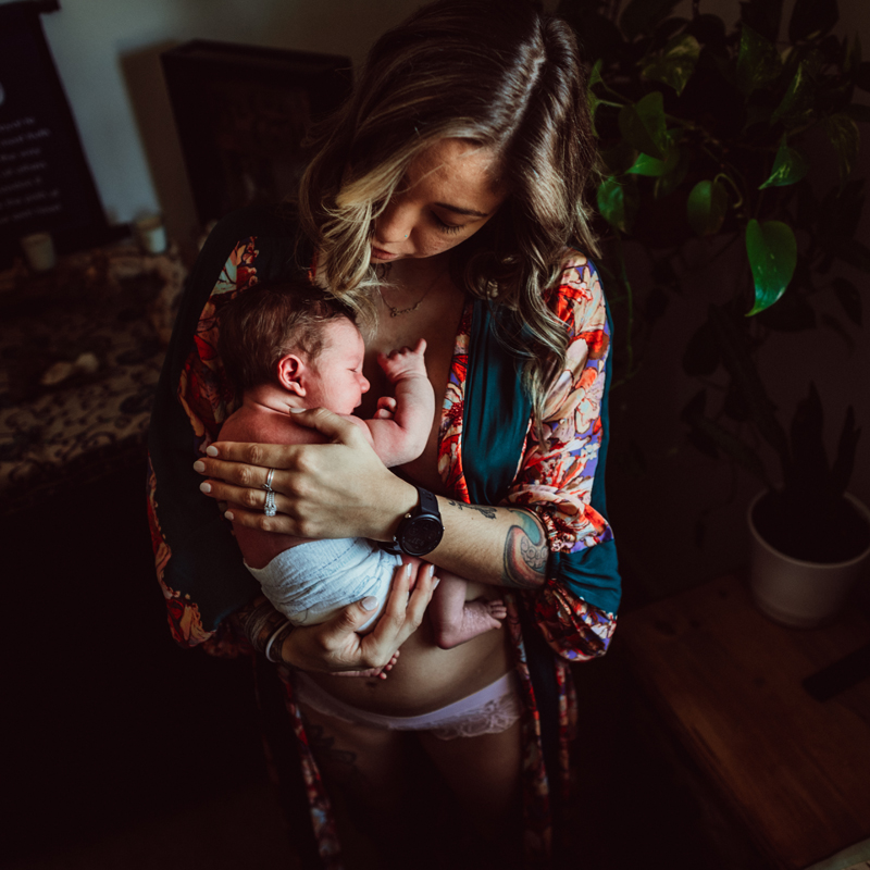 Postpartum Photography - a young woman consoles her young child as she holds baby close