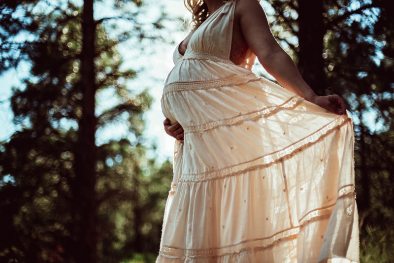 Maternity Photography - a woman in a dress holds her pregnant belly as she walks through the forest