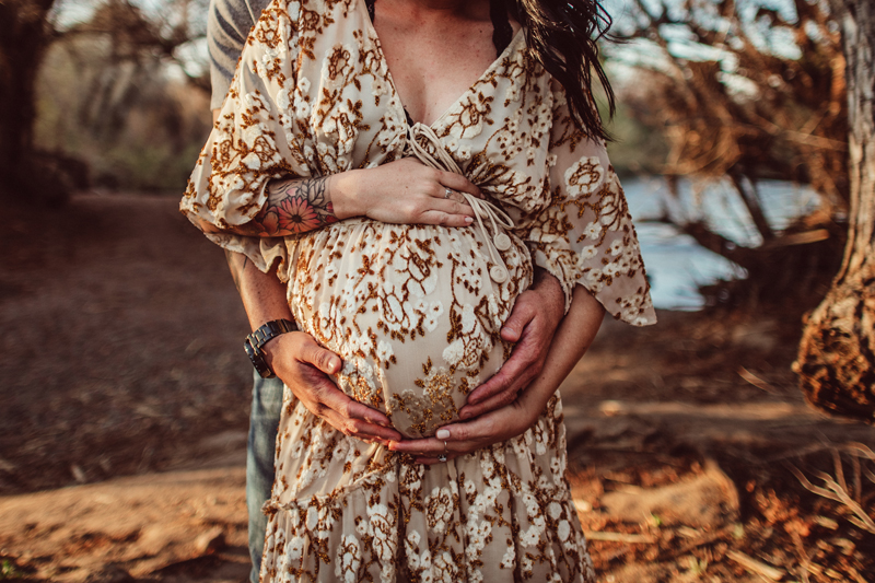 Maternity Photography - Man embraces expecting wife from behind, both their hands hold onto her pregnant belly softly