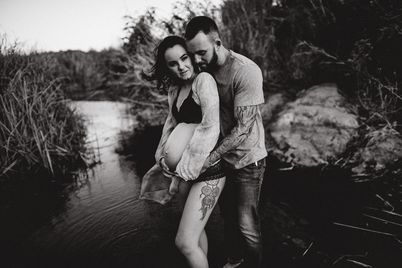 Maternity Photography - man and pregnant woman hold each other close, they stand in a quiet river