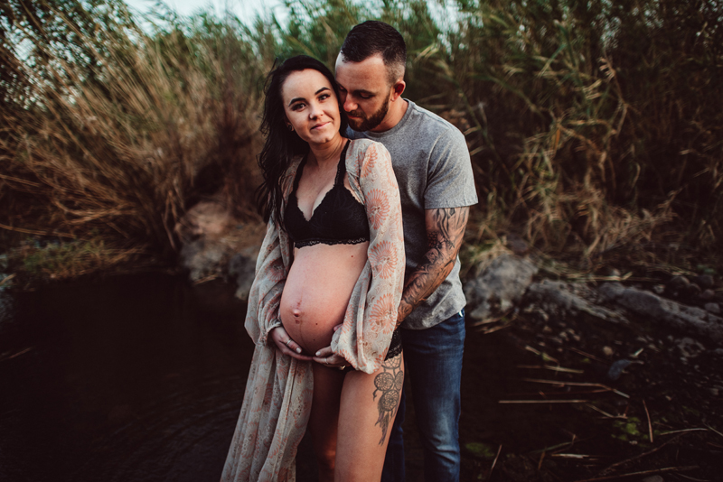 Maternity Photography - Woman embraced by her partner, she is pregnant, they stand outside