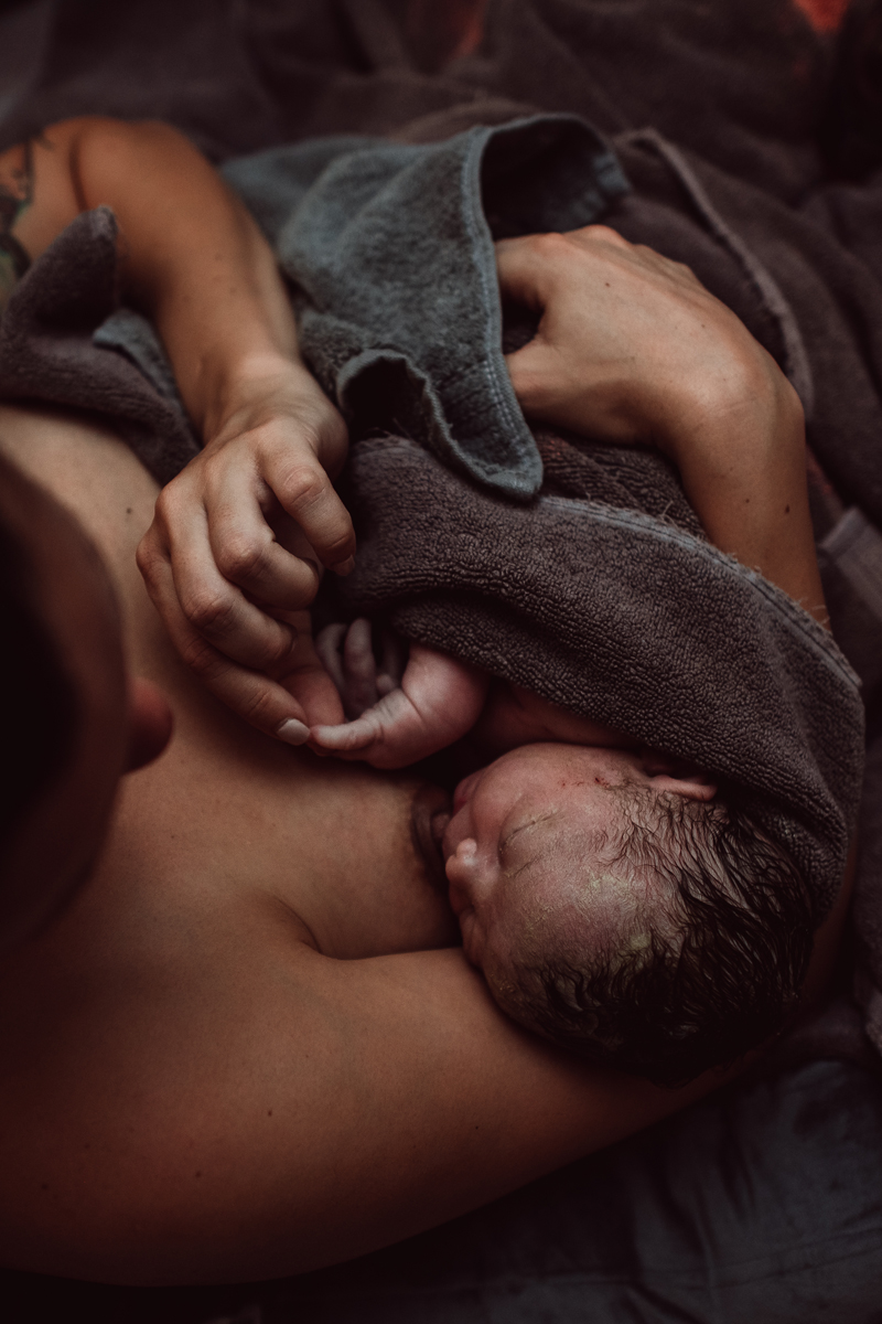 Birth Photography - new baby latches on to breastfeed as mom holds baby near chest