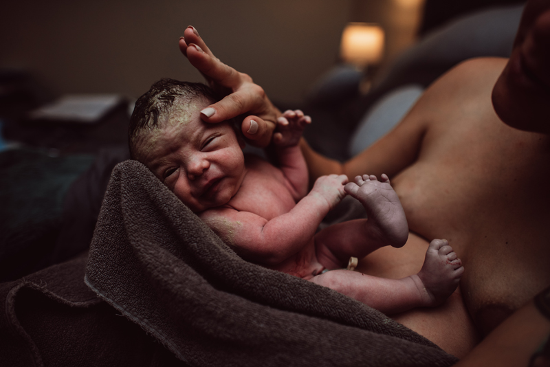 Birth Photography - Mom's hand gently soothes newborn baby being held in her arms