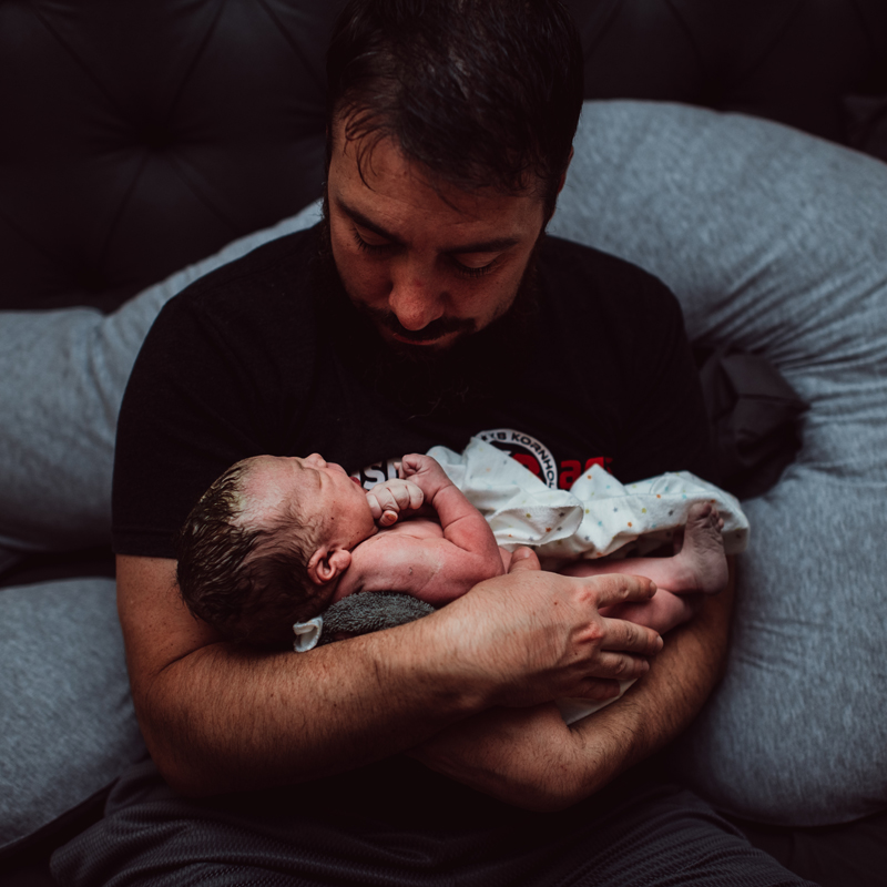 Birth Photography - a newborn baby is wrapped in a blanket and being held by dad