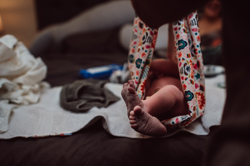 Birth Photography - a newborn baby's feet poke out of a decorative blanket to be wrapped for warmth