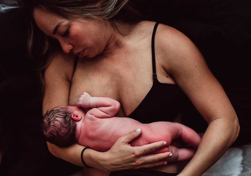 Birth Photography -Newborn baby being held by mom begins to breastfeed