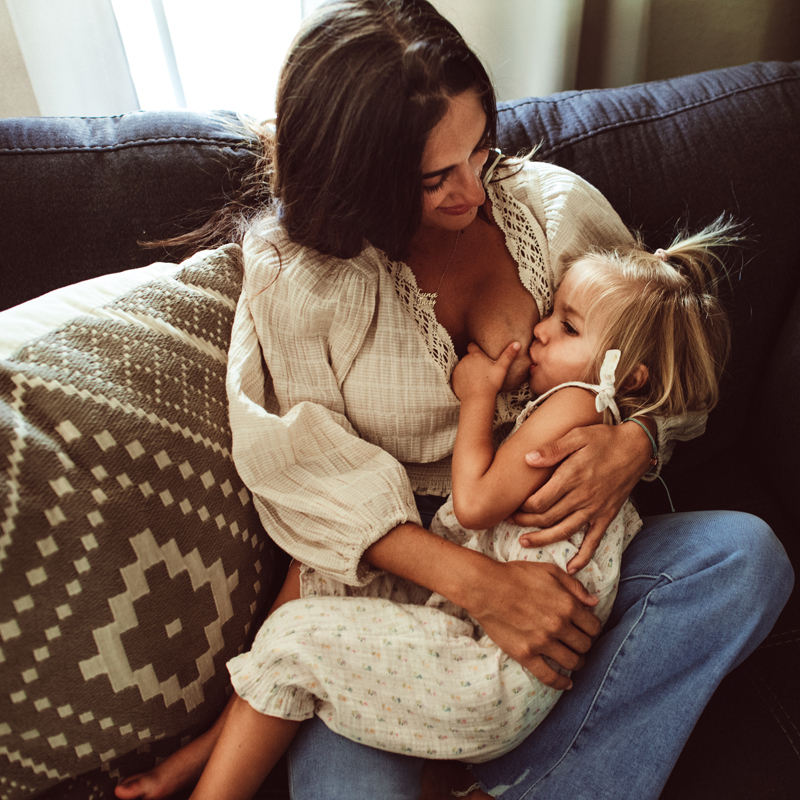 Family Photography - a young girl breastfeeds as her mom holds her on the couch