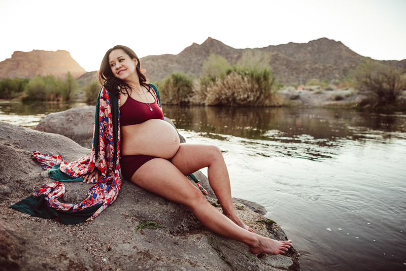 Maternity Photography - pregnant woman reclines outdoors on a rock near the river