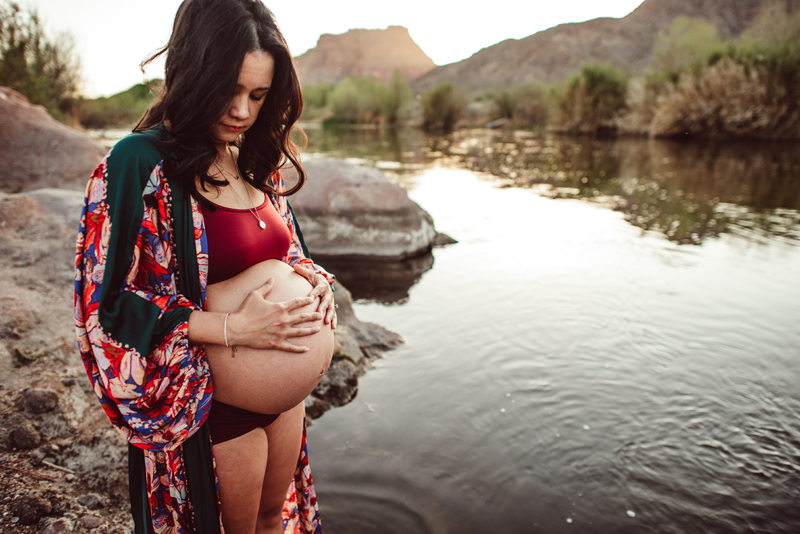 Maternity Photography - expecting woman holds her hands on her belly near the river bank