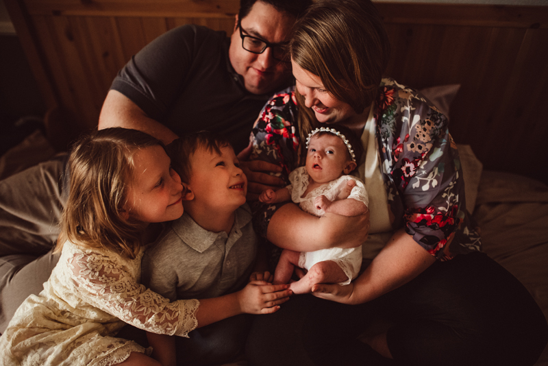 Family Photography - Mom holds newborn daughter, dad, brother, and sister lean in smiling
