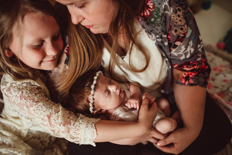 Family Photography - Mom holds baby as older sister hugs them both smiling
