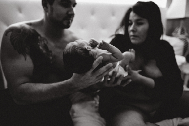 Postpartum Photography - a woman passes her newborn child to dad within their bedroom