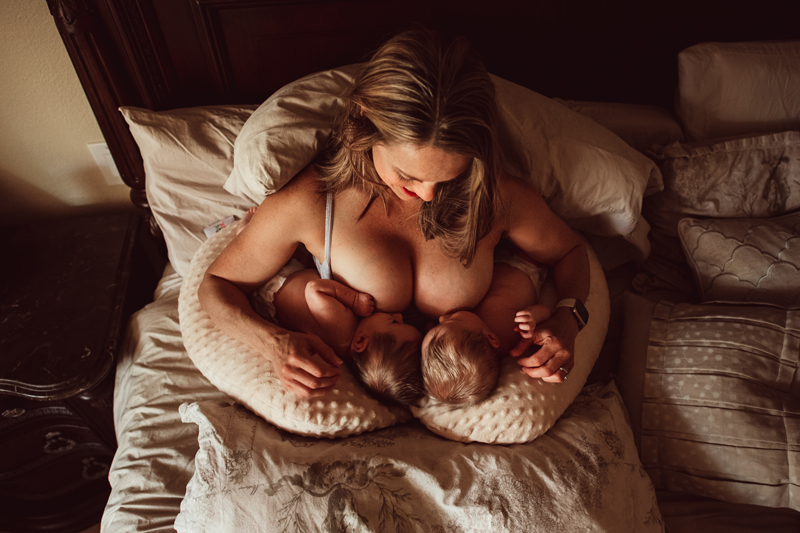 Postpartum Photography - a woman smiles as she looks down at her two breastfeeding newborn twins
