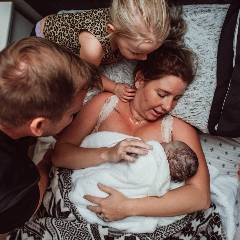 Birth Photography - Woman holds her new baby as her daughter and husband also look in