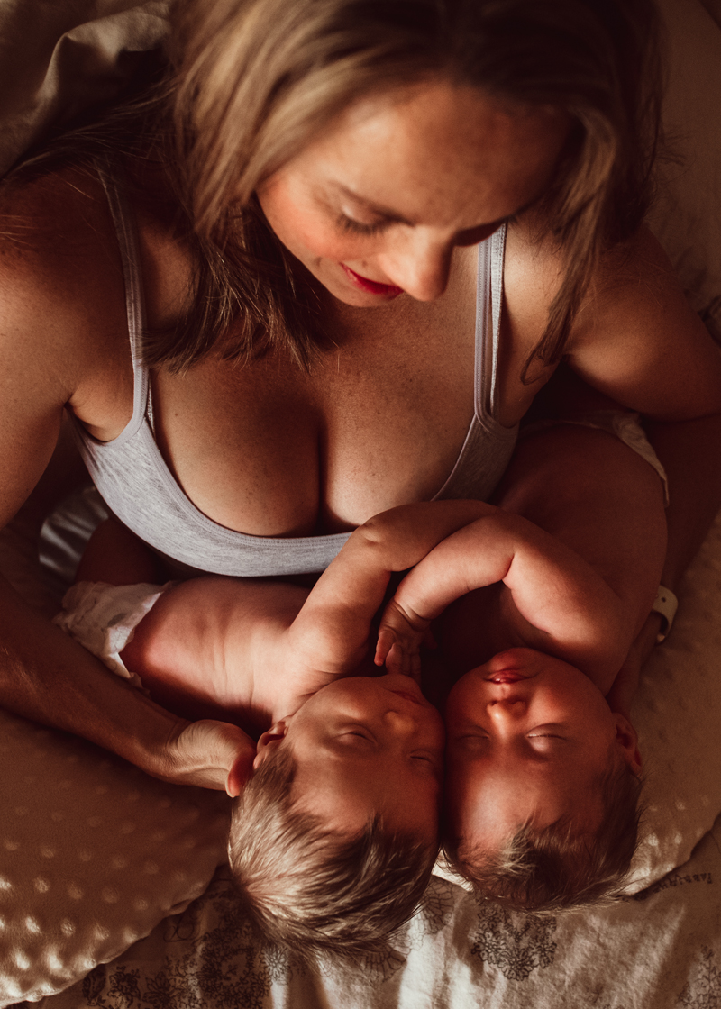 Postpartum Photography - a young mother holds both of her newborn twins closely with adoration as she sits