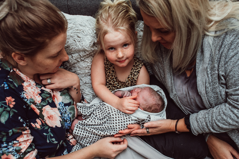 Birth Photography - Mom holds onto wrapped newborn baby with young daughter and grandmother, they're all content