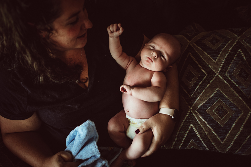 Postpartum Photography - A mother holds her young baby in her arms on the couch