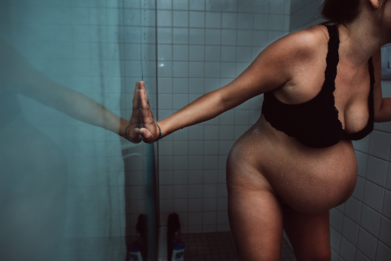 Birth Photography - pregnant woman ready for labor leans against shower walls,
