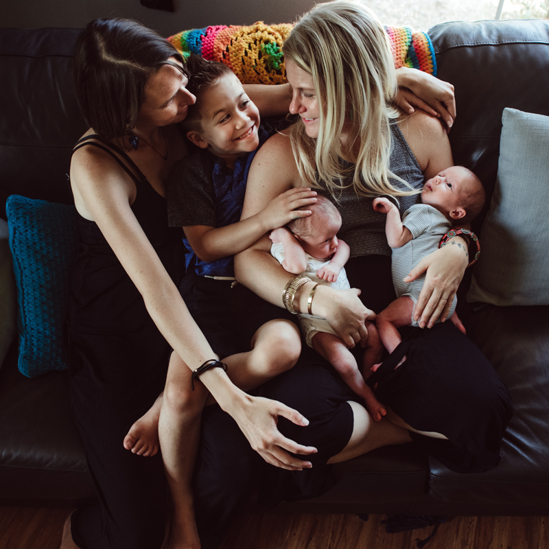 Postpartum Photography - a mother holds onto her two newborn twins, another embraces her and their young son