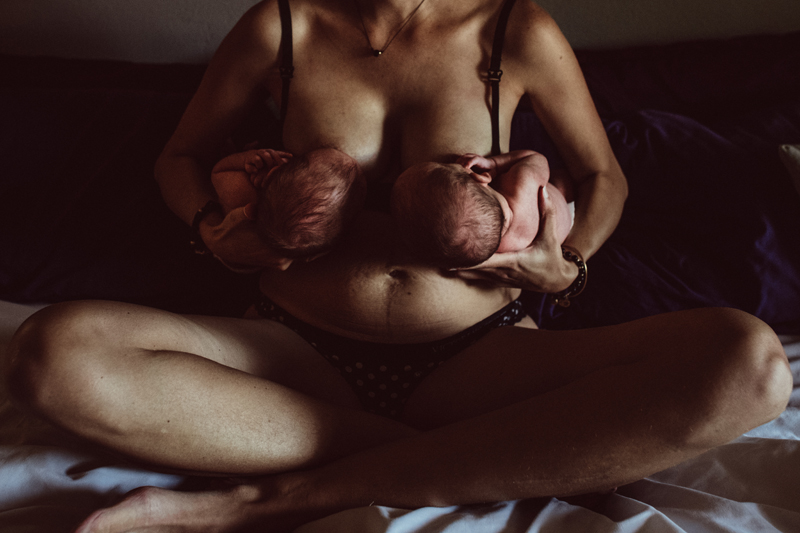 Postpartum Photography - a woman breastfeeds both of her twins, a baby in each of her arms