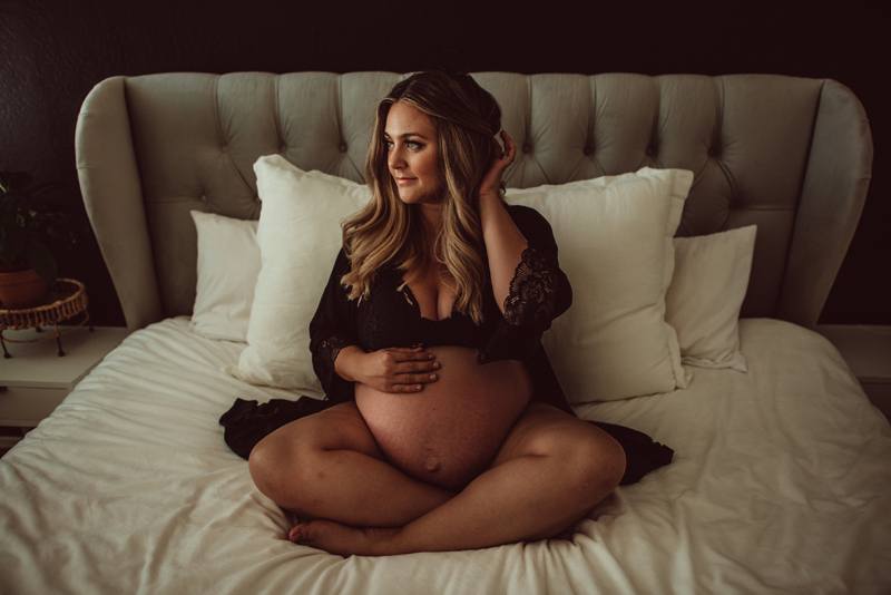 Maternity Photography - expecting mother places hand on her belly as she sits comfortably on her bed