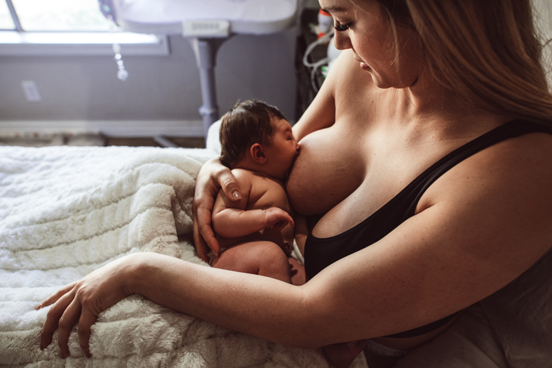 Postpartum Photography - a woman breastfeeds her young baby from bed