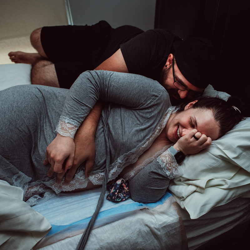 Birth Photography -woman smiles while in labor, her partner leans into her also smiling