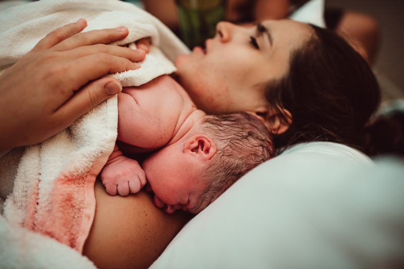 Birth Photography -woman just gave birth and holds baby near her shoulder as she rests