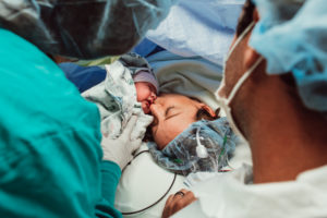 mother kisses baby after cesarean birth in operating room